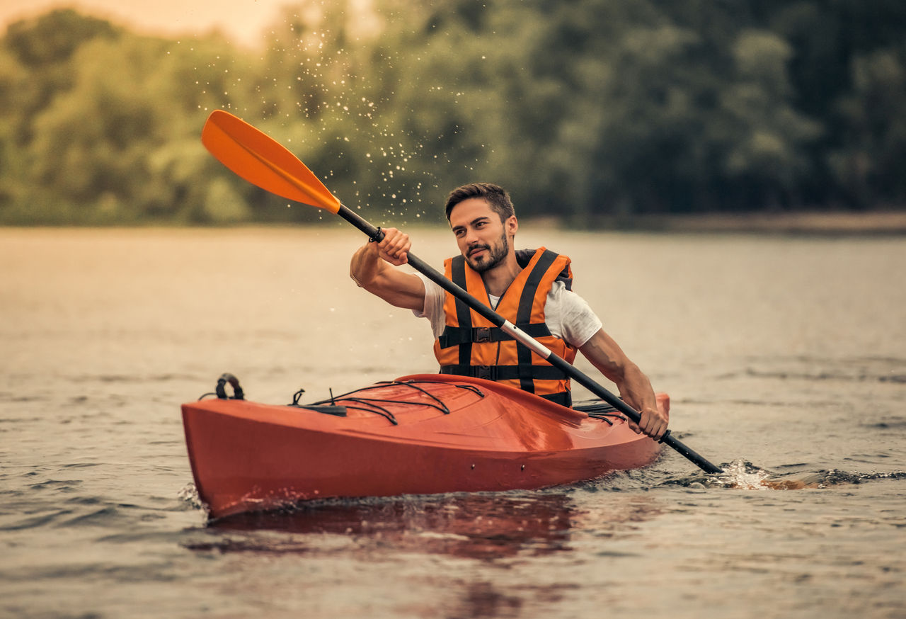 Handsome young man in sea vest is smiling while sailing a kayak